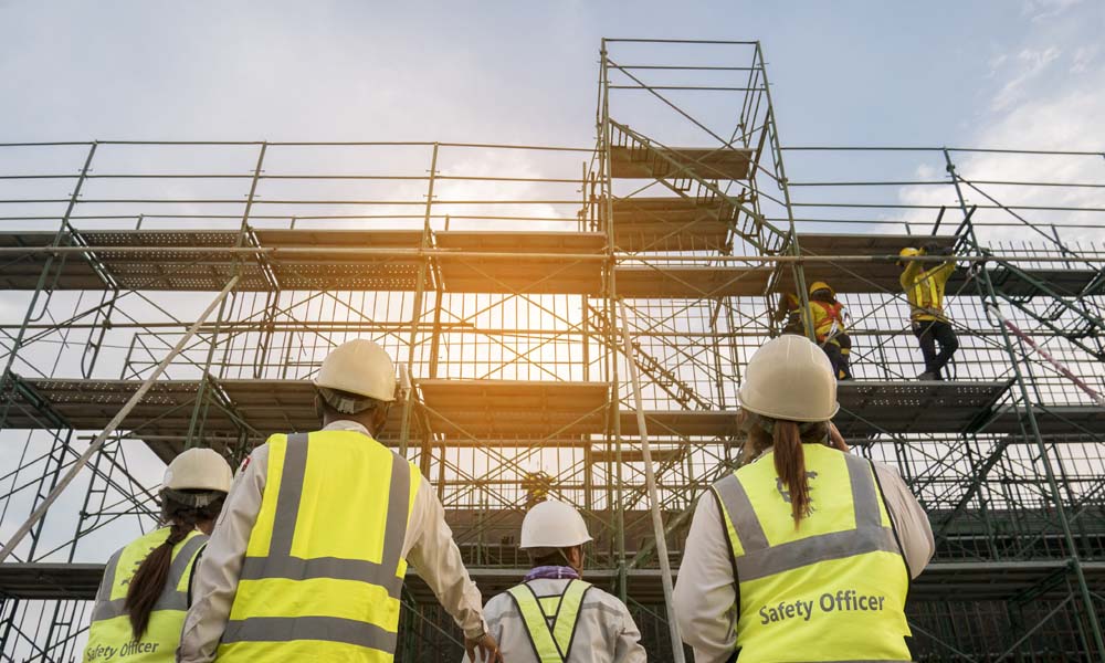 Construction Risk Advisor - Protect Your Employees With Ladder Alternative Programs - Group of Construction Workers Looking up to Scaffolding With a Sunrise Backdrop